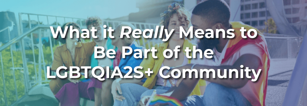 Group of LGBTQIA2S+ friends at an outdoor event holding pride flags, with headline overlay: “What it Really Means to Be Part of the LGBTQIA2S+ Community.”